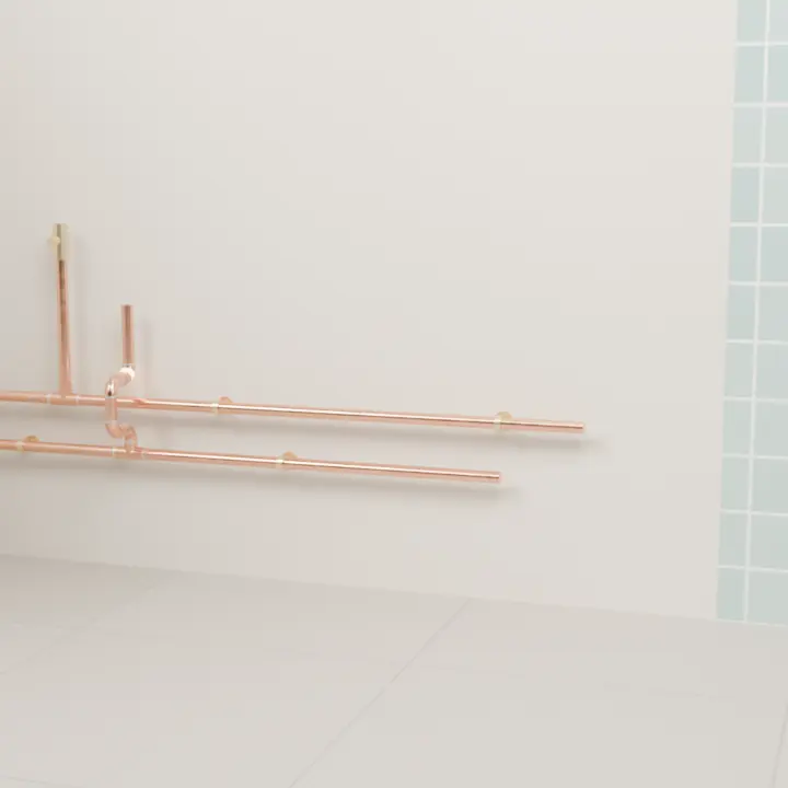 Gros plan : les tubes de cuivre posés le long du mur, coudes brasés et colliers en laiton